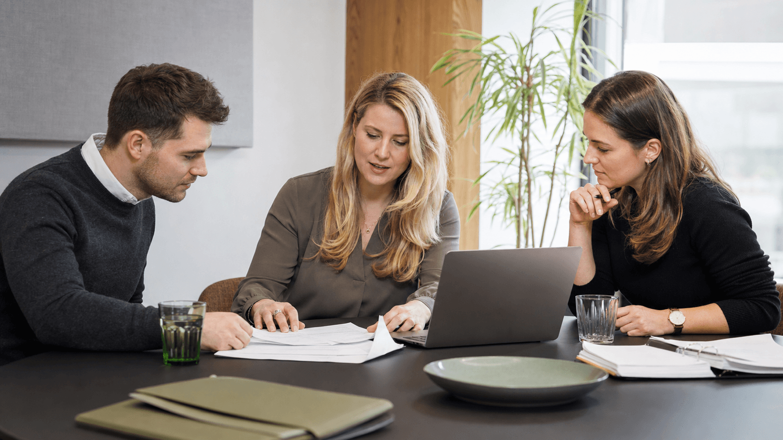 Blonde Finanzverantwortliche erklärt zwei Kollegen einen KI-gestützten Rechnungsworkflow in einem österreichischen Dienstleistungsbetrieb